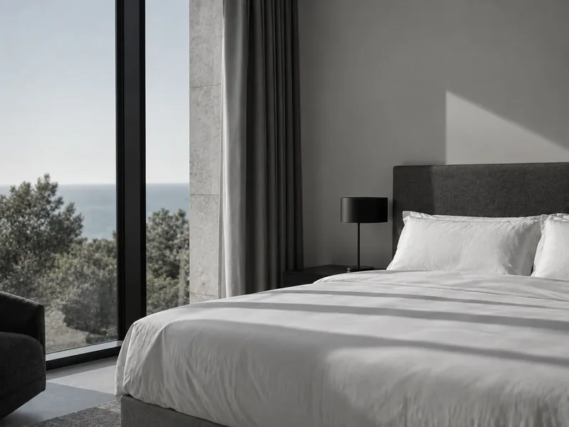 A made bed by a floor-to-ceiling window with a sea view